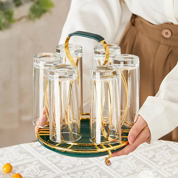 Set of clear glasses with gold rims on a green tray held by a person.
