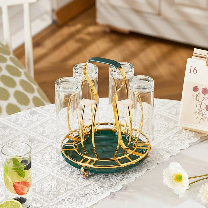 Set of six clear glasses with a gold and green holder on a table with a white tablecloth.
