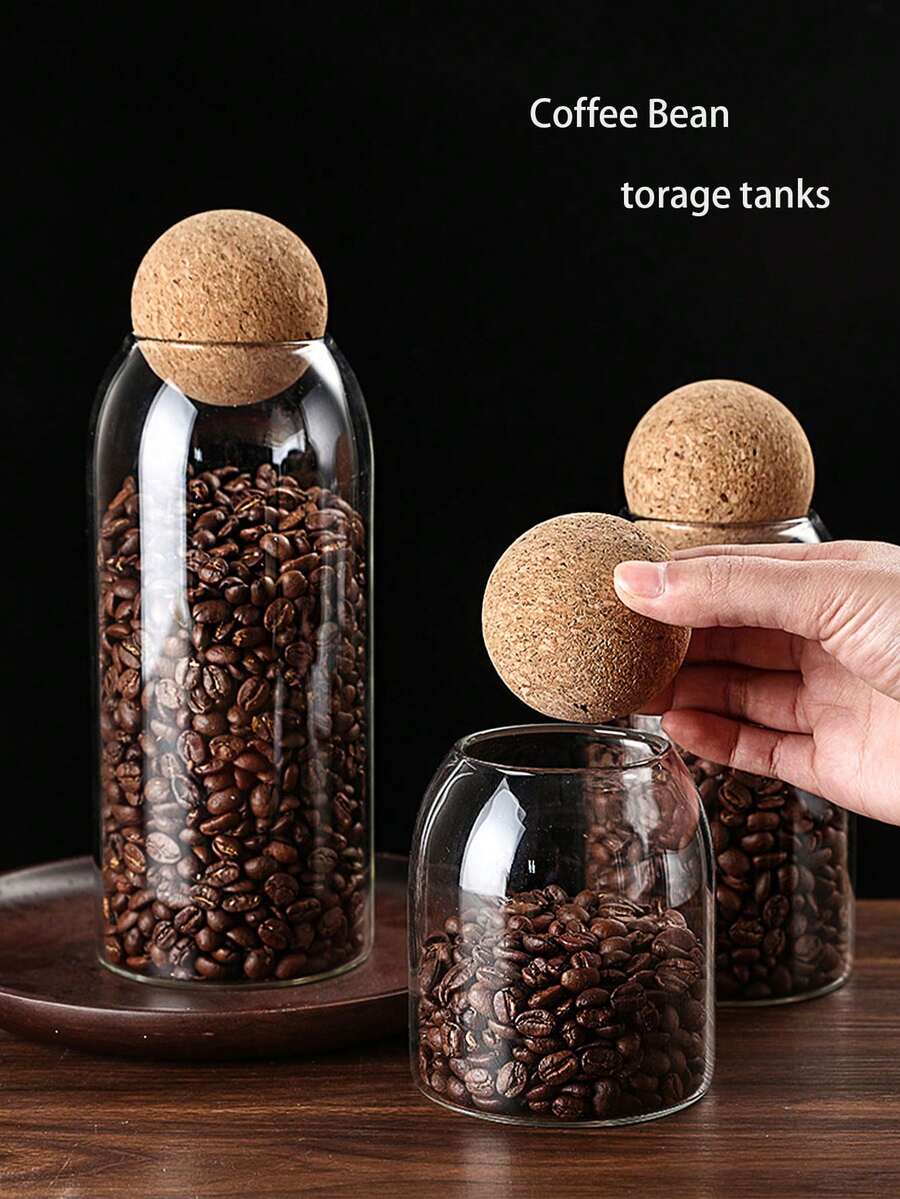 Glass storage tanks filled with coffee beans, topped with cork lids, on a wooden surface.