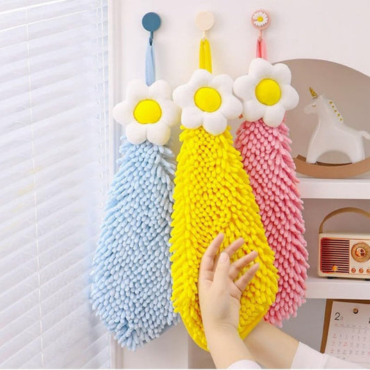 Three colorful daisy-shaped cleaning brushes hanging on a hook with a hand reaching out to grab one.