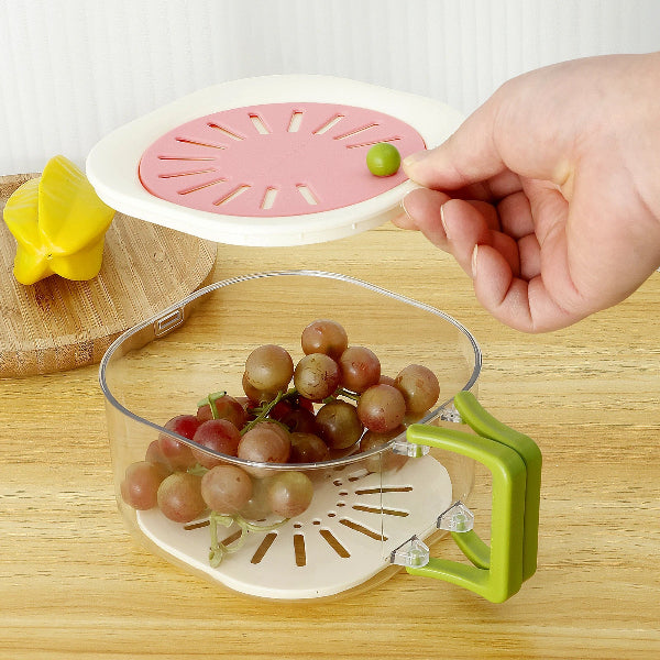 Hand placing a grape into a clear fruit drainer with pink lid on a wooden surface.