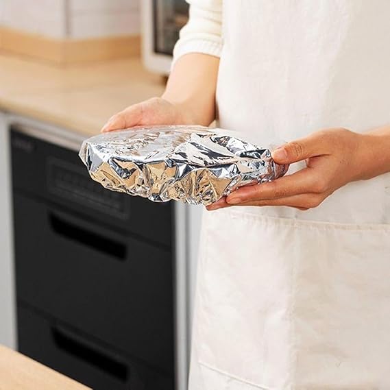 Person holding a dish wrapped in aluminum foil in a kitchen setting