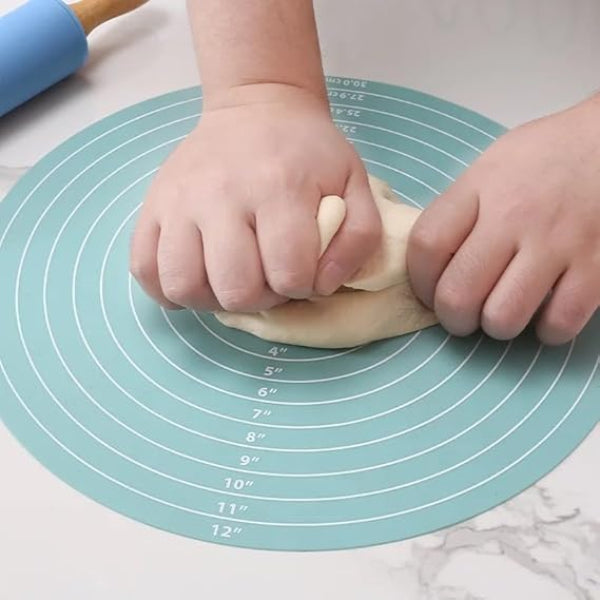 Child's hands kneading dough on a silicone baking mat with measurements.