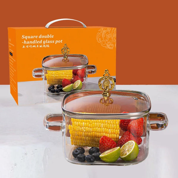 Square double-handled glass pot with fruits and vegetables inside, next to an orange product box.