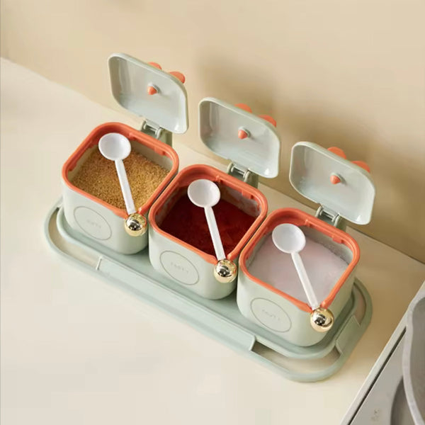Set of three spice containers with lids and spoons on a beige surface
