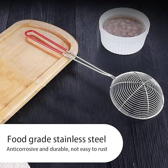 Metal strainer with red handle on a dark surface, next to a wooden board and small container.