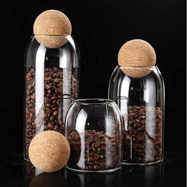 Glass jars with cork lids containing coffee beans on a black background