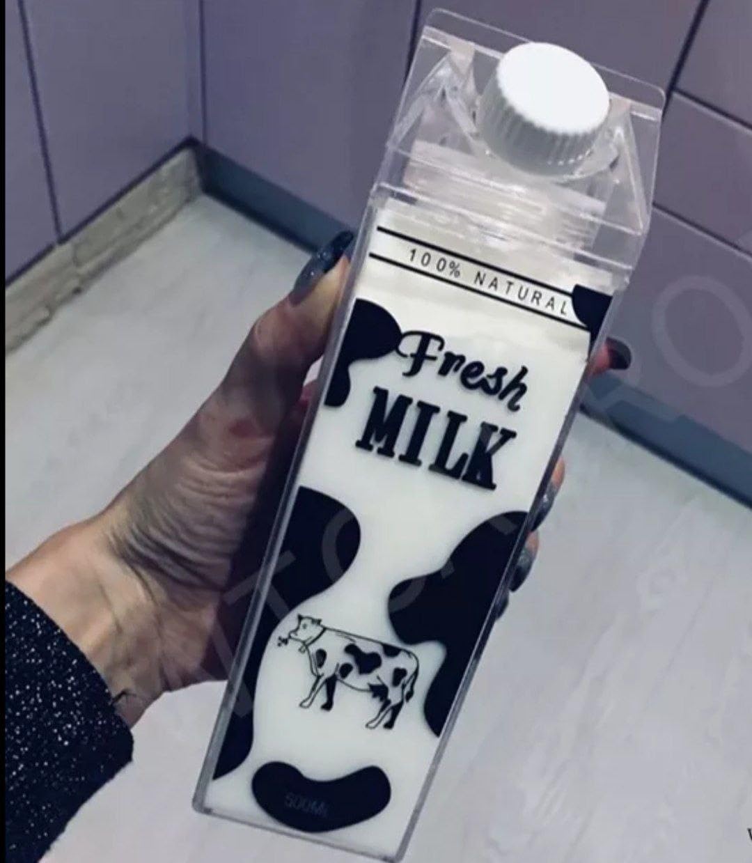 Hand holding a transparent container with 'Fresh Milk' text and cow design against a tiled wall background.