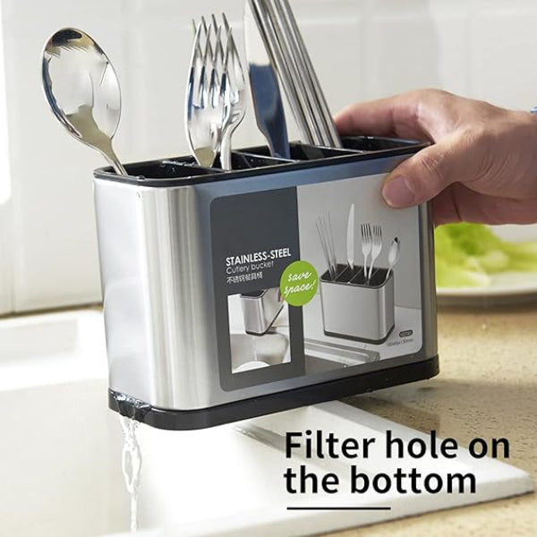 Stainless steel utensil holder with a hand holding it, placed on a kitchen counter.
