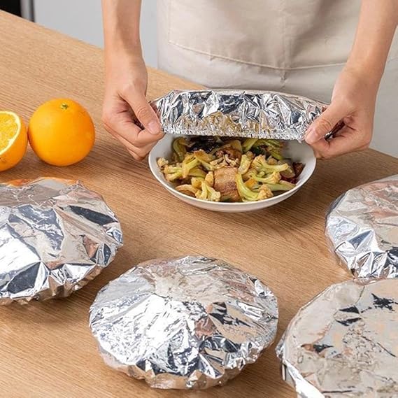 Person unwrapping a foil-wrapped dish on a wooden table with oranges in the background