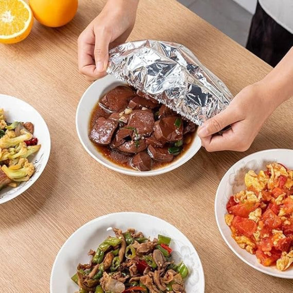 Person opening a foil-wrapped dish on a table with other plates of food.