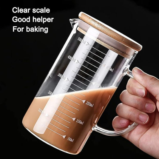 Glass measuring cup with wooden lid held by a hand, filled with a brown liquid, on a black background.