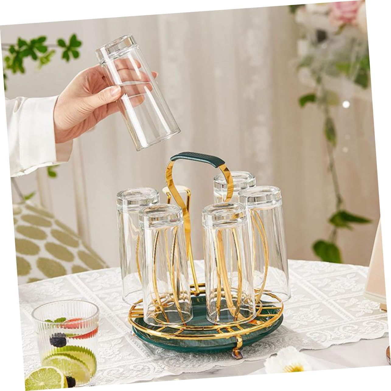 Clear glass cups with gold handles on a green stand, held by a hand against a blurred indoor background.