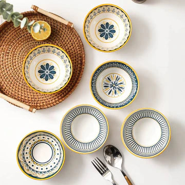 Set of ceramic plates with decorative patterns on a white surface, surrounded by a woven basket and cutlery.