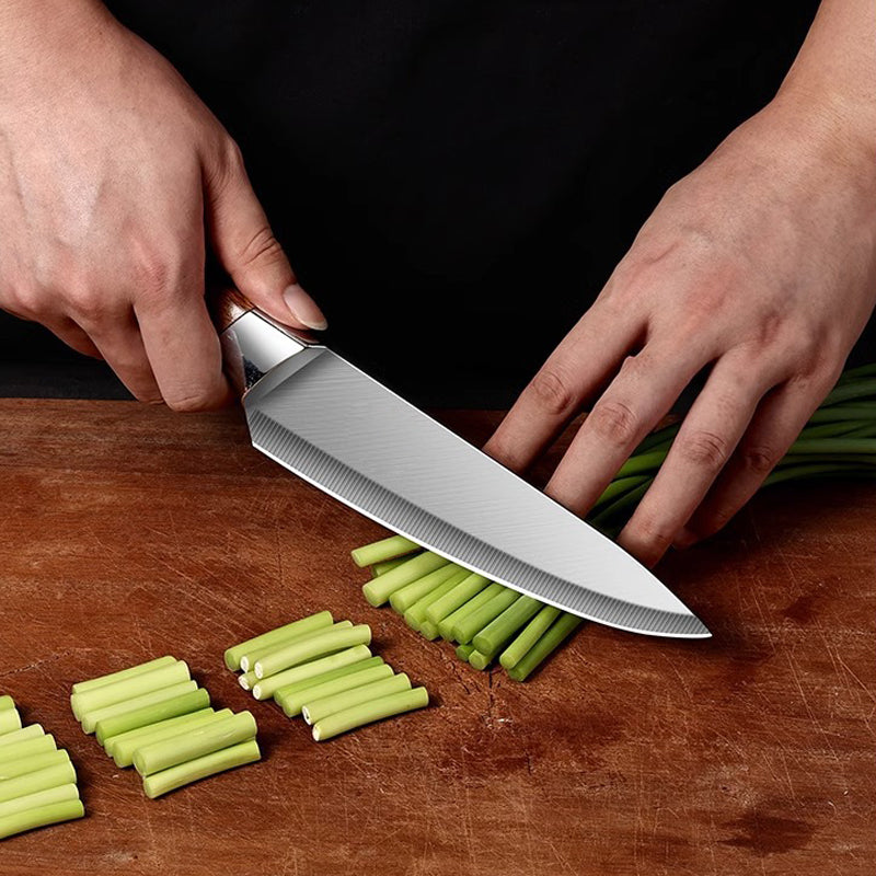 Person using a chef's knife to slice green vegetables on a wooden cutting board.