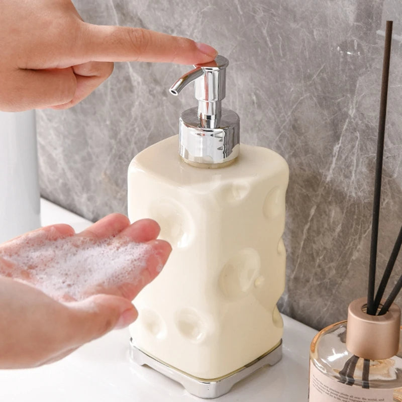 Person using a textured soap dispenser with soapy hands, marble wall background