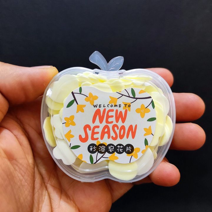 Hand holding a small container of white items with a 'Welcome to New Season' label against a black background