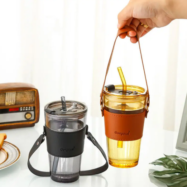 Two travel mugs with straws on a table with a radio and plant in the background.