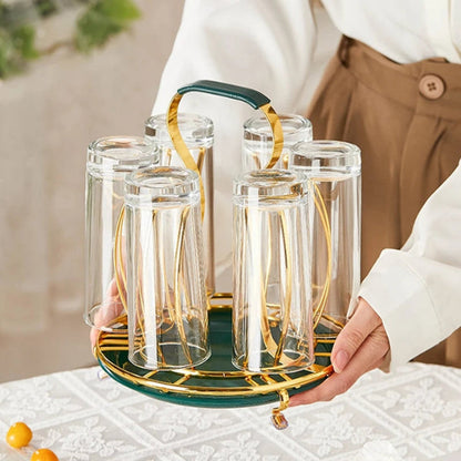 Set of clear glasses with gold rims on a green tray held by a person.