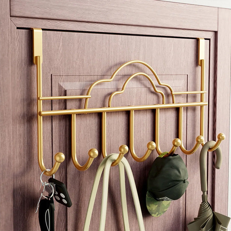 Gold over-the-door hook rack with keys, cap, and umbrella on a wooden door.