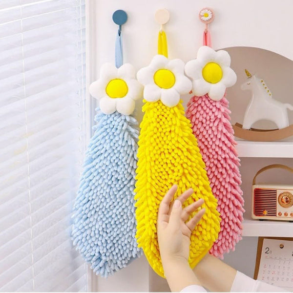 Three colorful daisy-shaped cleaning brushes hanging on a hook with a hand reaching out to grab one.