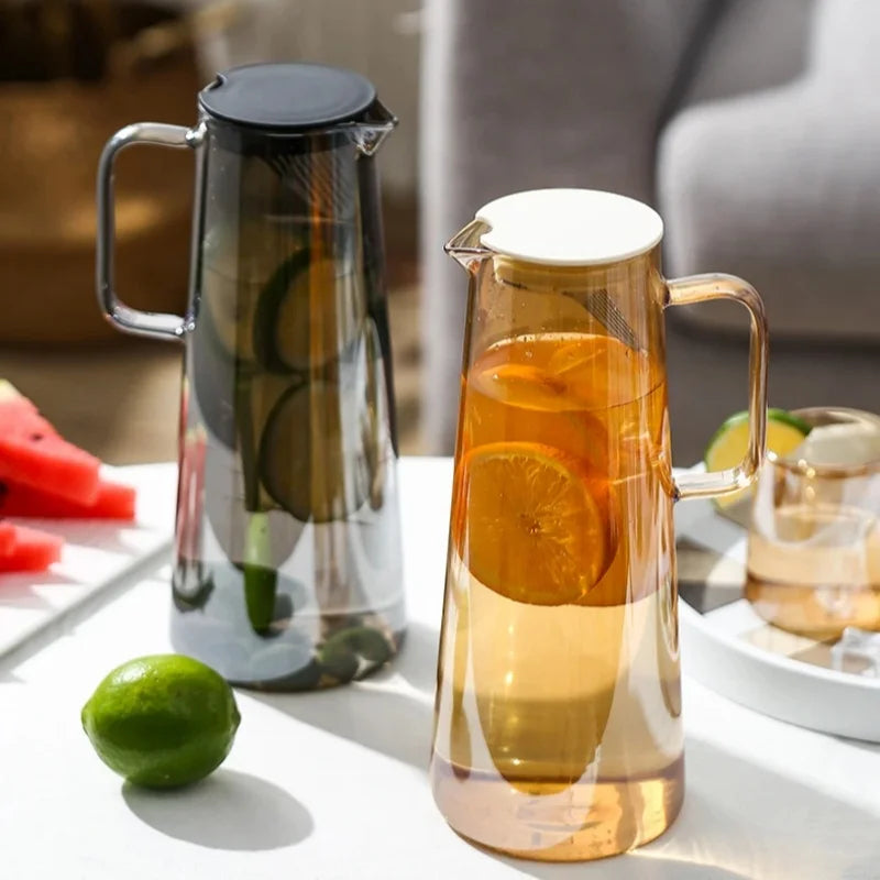 Two glass pitchers on a table with fruit and a blurred background