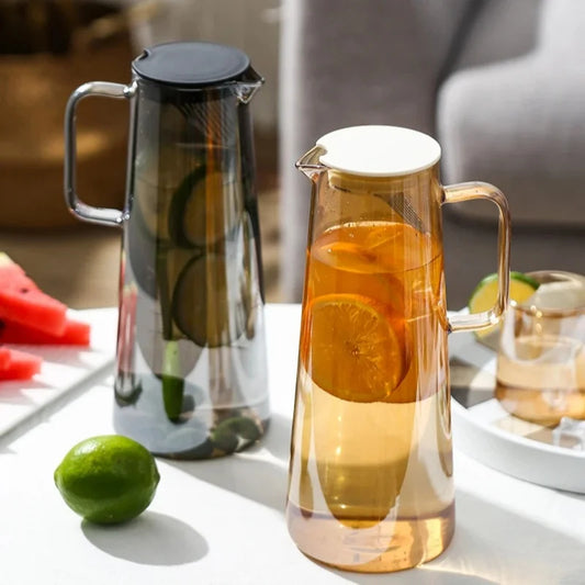 Two glass pitchers on a table with fruit and a blurred background