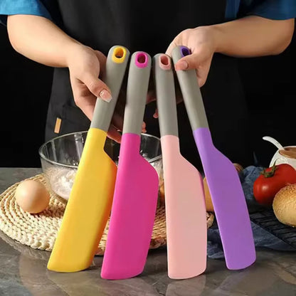 Four colorful spatulas held by a person with kitchen items in the background