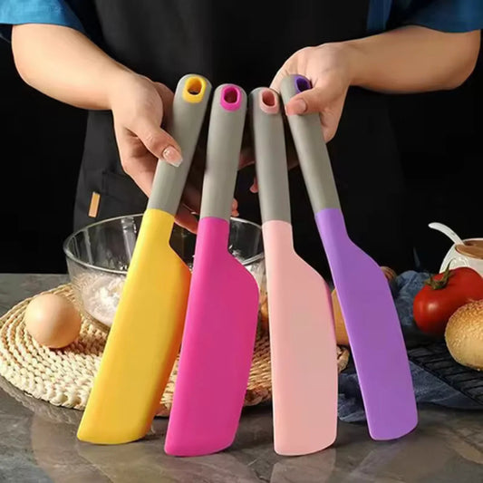 Four colorful spatulas held by a person with kitchen items in the background