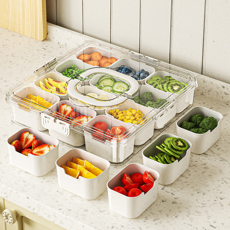 Transparent food storage container with compartments filled with various fruits and vegetables on a marble surface.