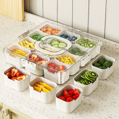 Transparent food storage container with compartments filled with various fruits and vegetables on a marble surface.