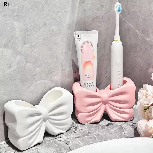 Two bow-shaped holders with a tube of toothpaste and a toothbrush on a bathroom counter.