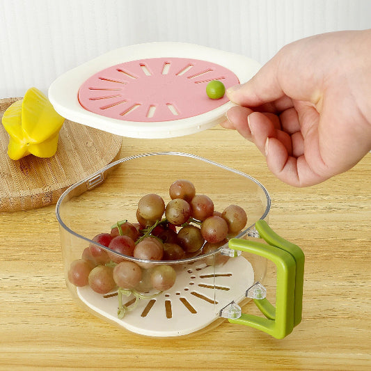 Hand placing a grape into a clear fruit drainer with pink lid on a wooden surface.