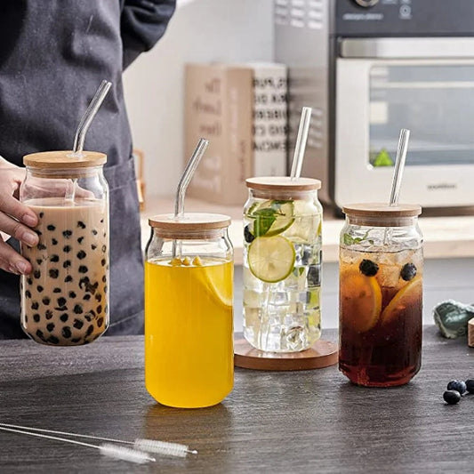 Four glass jars with wooden lids and straws containing different beverages on a kitchen counter.