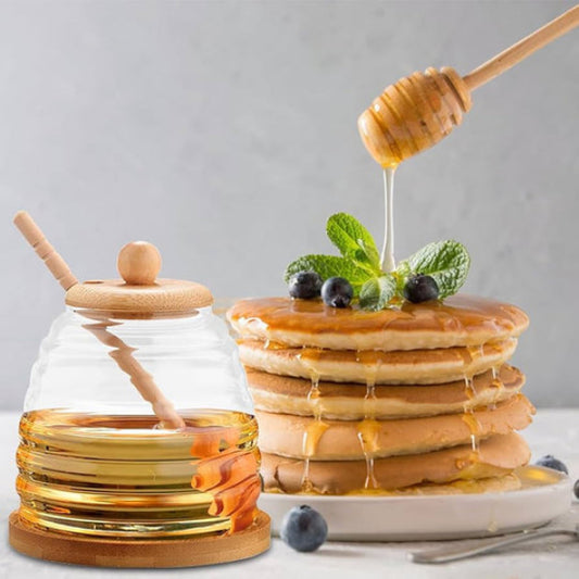 Glass honey jar with wooden dipper next to a stack of pancakes with honey and blueberries.