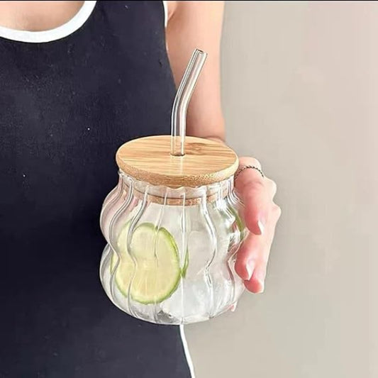 Glass jar with a wooden lid and straw, containing sliced cucumbers and ice, held by a person.