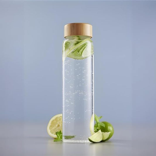 Clear glass bottle with wooden cap containing water and lime slices on a light gray background