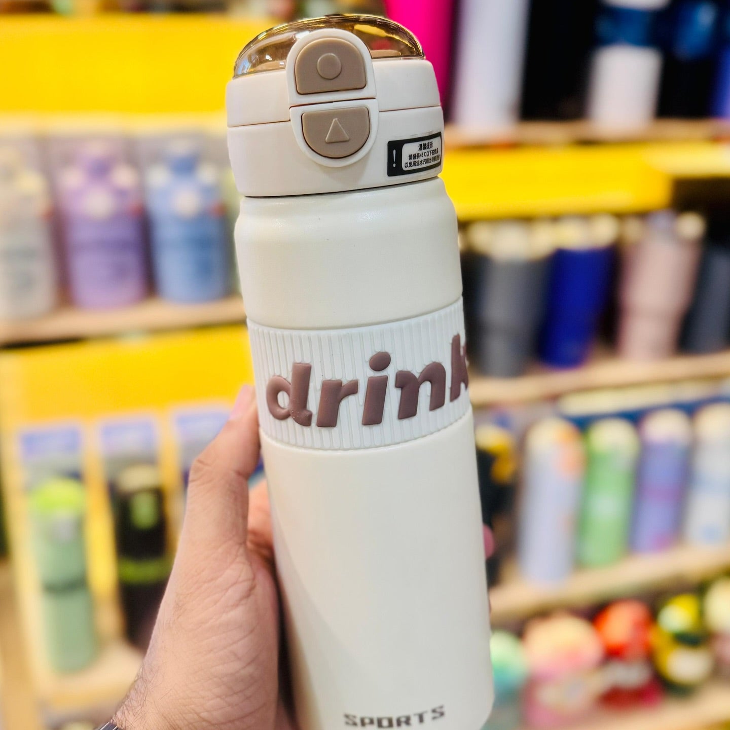 White insulated bottle with 'drink' text held in a hand against a store shelf background