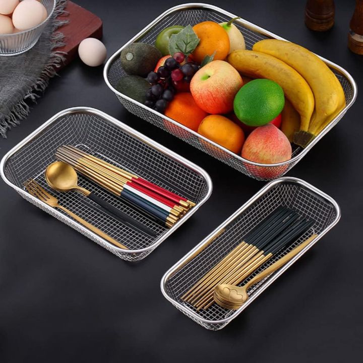 Three mesh trays with cutlery and fruits on a dark surface