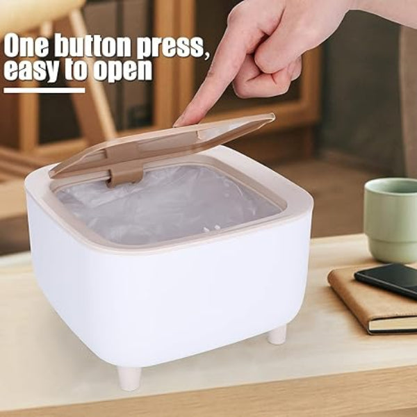 Hand opening a white trash bin with a beige lid on a wooden surface.