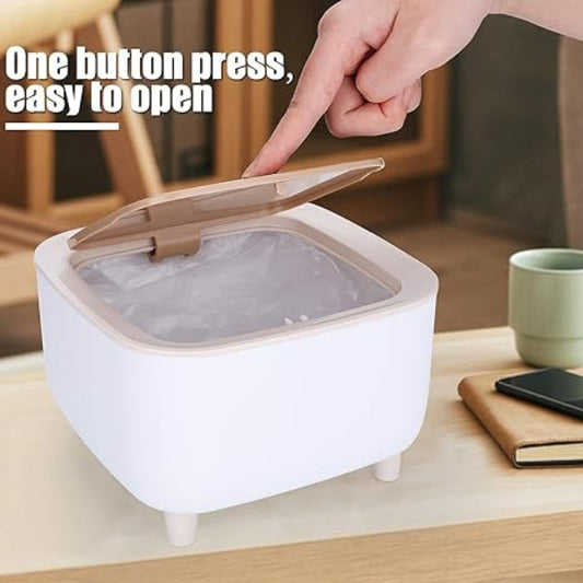 Hand opening a white trash bin with a beige lid on a wooden surface.