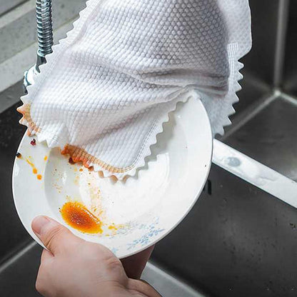 Hand holding a white plate with food residue over a sink, with a white towel draped over the edge of the sink.