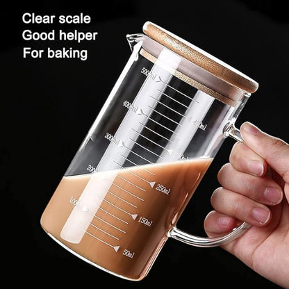 Glass measuring cup with wooden lid held by a hand, filled with a brown liquid, on a black background.