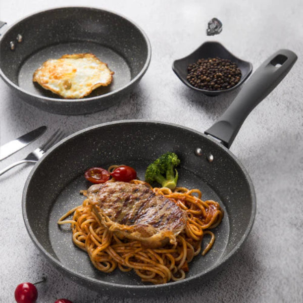 Fried egg, steak, and spaghetti on a black frying pan with a small dish of pepper and cherry tomatoes.