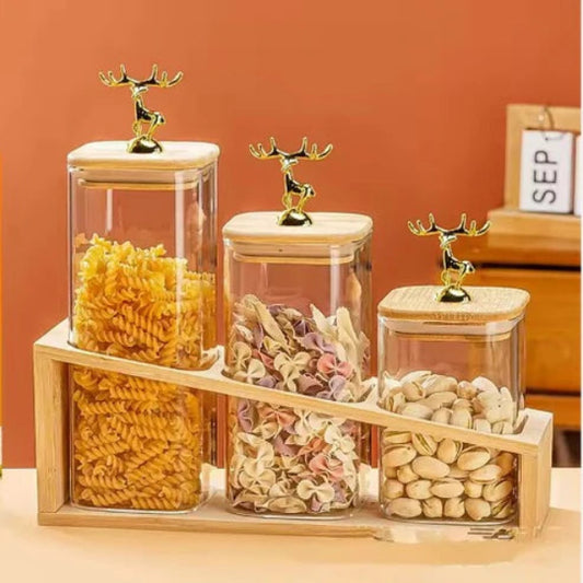 Set of glass jars with wooden lids containing various pasta and nuts on a wooden stand against an orange wall.