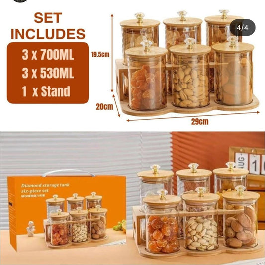 Glass storage jars with wooden stands and included items displayed on a table.