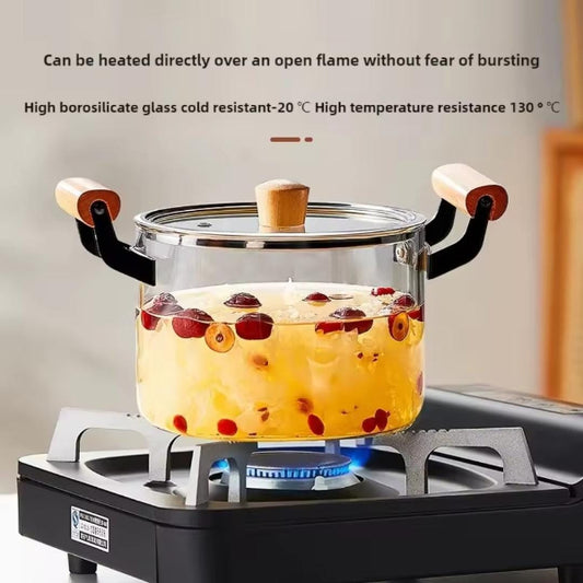 Glass pot with handles on a gas stove, containing a hot beverage with fruits.