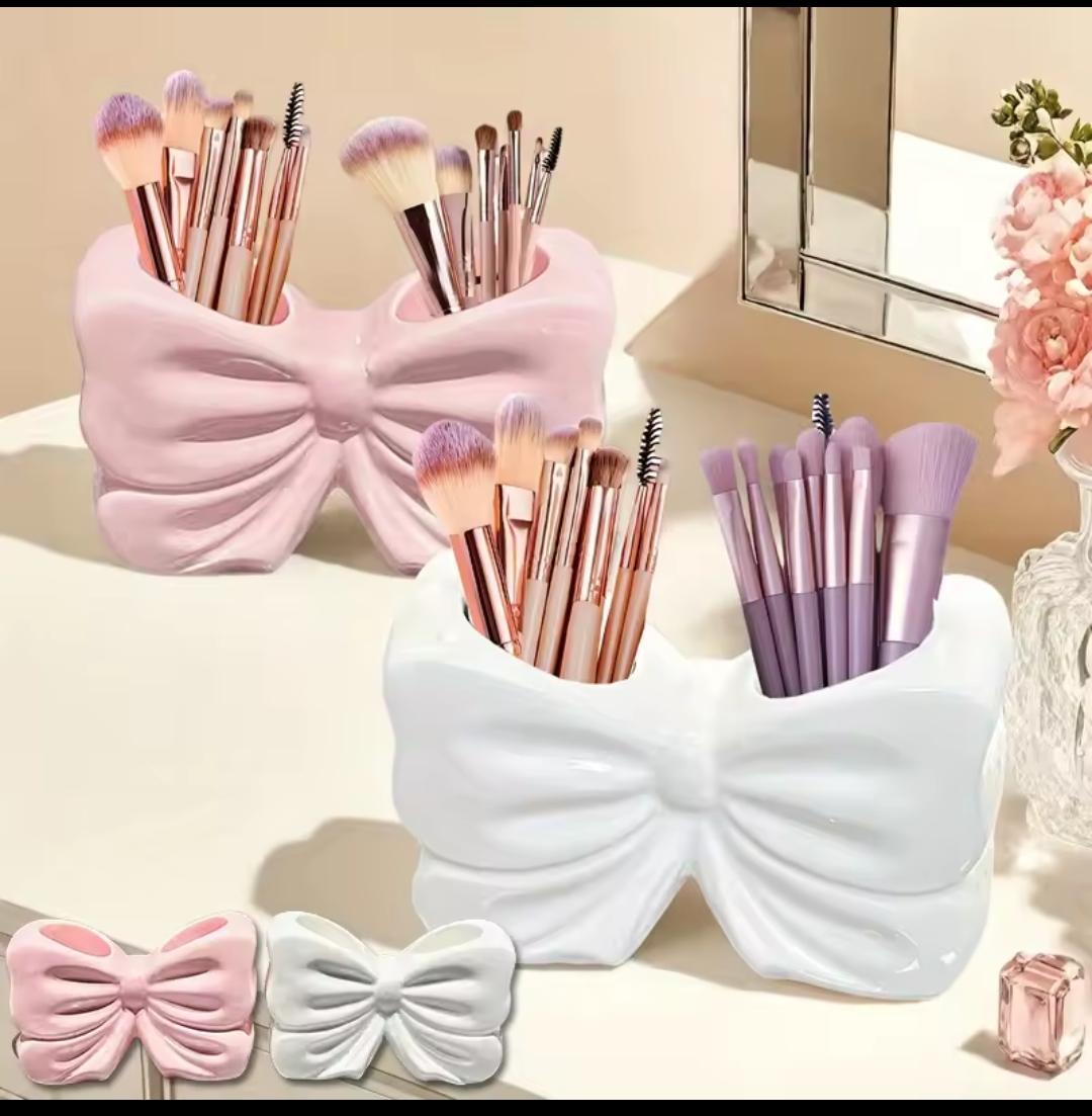 Makeup brushes in pink and white bow-shaped holders with a mirror and flowers in the background.