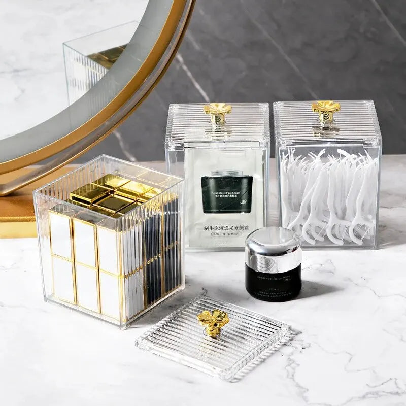 Set of skincare products in clear containers with gold accents on a marble surface.