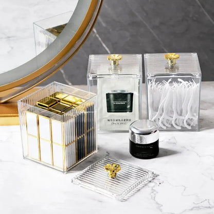 Set of skincare products in clear containers with gold accents on a marble surface.